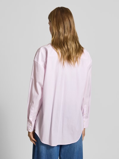 Frauenmodel trägt Oversized Hemdbluse mit Brusttasche von Guess Jeans, reine Baumwolle, Oversized-Fit, zart rosafarben, vertikale Streifen, Logo-Patch, langärmelig, Hemdblusenkragen, durchgehende Knopfleiste, abgerundeter Saum, verlängerter Rücken, Ganzkörperansicht Rückansicht.