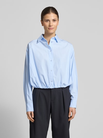 Frauenmodel trägt Cropped Bluse mit Hemdblusenkragen Modell 'Emmana' von Neo Noir aus reiner Baumwolle in Hellblau, lockere Passform, Knopfleiste, Langarm, Ganzkörperansicht von vorne.