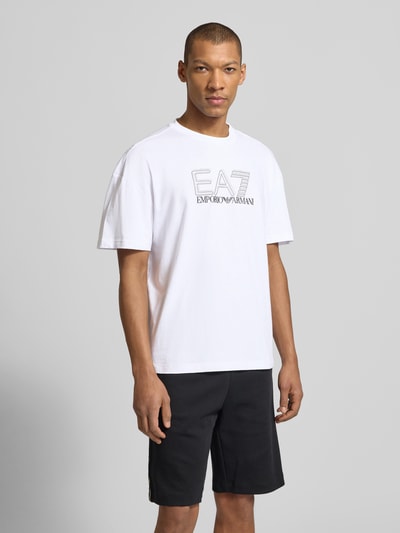 Męski model nosi T-shirt mit Logo und Rundhalsausschnitt von EA7 Emporio Armani, bawełna, krój regular fit, długość tyłu 68 cm, Ganzkörperansicht z przodu.