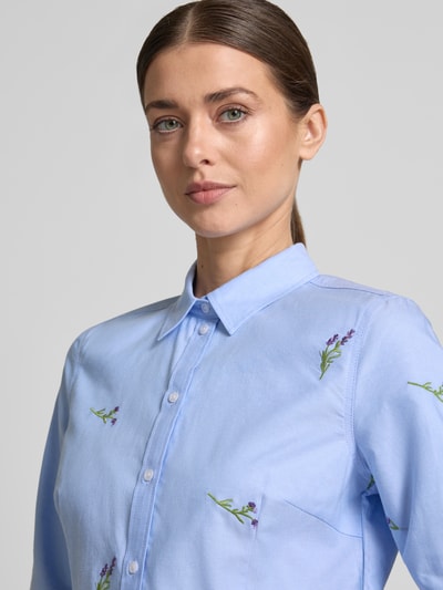 Modelka kobieca ma na sobie Hemdbluse mit Motiv-Stitchings od Christian Berg Woman, bawełna, krój prosty, błękitny kolor, kołnierzyk kent, gładka faktura, haftowane motywy, długość tyłu i rękawa 62 cm w rozmiarze 36, widok na górną część ciała z przodu