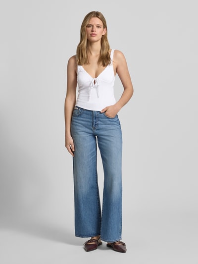 Vrouwenmodel draagt Slim Fit Top mit Spitzenbesatz van Guess Jeans, wit, elastische katoenmix met modal, kant en strik, mouwloos, v-hals, slim fit. Ganzlichaamsaanzicht van voren.