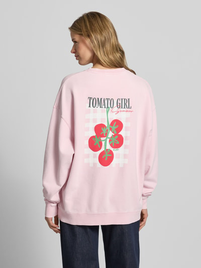 Frauenmodel trägt Oversized Sweatshirt mit rückseitigem Statement-Print von OH APRIL in Rosa mit Kirschtomatenmotiv auf Baumwolle, Ganzkörperansicht Rückansicht.