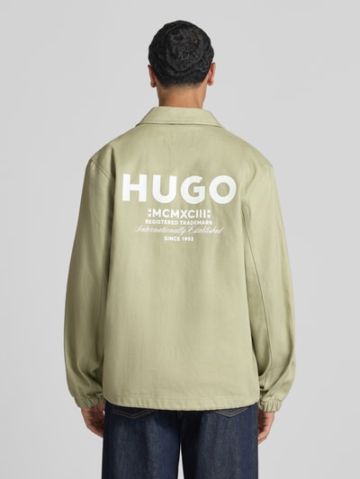 Männermodel trägt Regular Fit Bomberjacke / Blouson aus reiner Baumwolle Modell 'Biyo2631' von HUGO Blue in Hellgrün, Ganzkörperansicht Rückansicht.