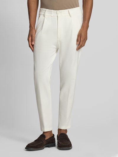 Männermodel trägt Slim Fit Stoffhose mit Bundfalten Modell 'Chasy' von Drykorn in Creme aus Baumwoll-Mix, Eingrifftaschen, Ganzkörperansicht von vorne.