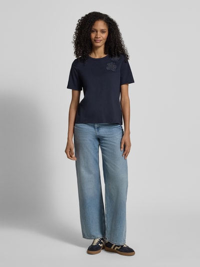 Frauenmodel trägt T-Shirt mit floralen Applikationen und Rundhalsausschnitt von Christian Berg Woman Selection im Regular Fit aus Baumwoll-Elasthan-Mix, dunkle Farbe, schlichte Struktur, Ganzkörperansicht von vorne.