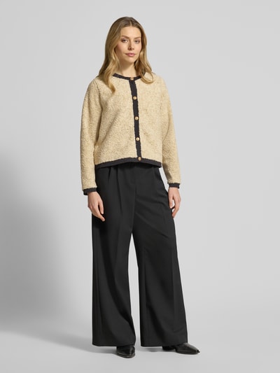 Frauenmodel trägt Strickjacke mit Knopfleiste Modell 'BESSIE' von Soyaconcept, beige, schwarze Knopfleiste, Regular Fit, Rundhalsausschnitt, gerippte Abschlüsse, weiche Textur, kombiniert mit schwarzer weiter Hose, Ganzkörperansicht von vorne.