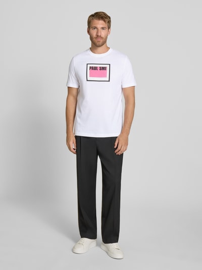 Männermodel trägt T-Shirt mit Label-Print von Paul Smith in Weiß mit schwarzer Hose, Regular Fit, Rundhalsausschnitt, Ganzkörperansicht von vorne, reine Baumwolle, Rückenlänge bei Größe M 71 cm.
