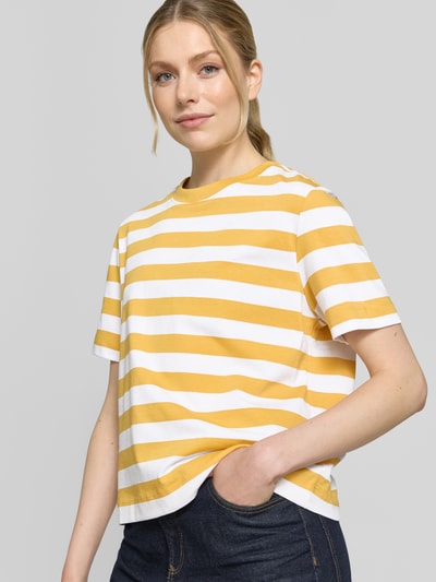 Frauenmodel trägt Boxy Fit T-Shirt aus reiner Baumwolle Modell 'ESSENTIAL' von Selected Femme, Optik:Allover-Muster, Gestreift, Rundhals, Kurzarm, heavy Jersey, Label-Patch, gelbe und weiße Streifen, Ganzkörperansicht von vorne.