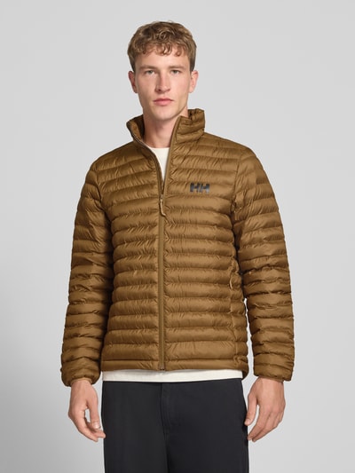 Männermodel trägt Steppjacke mit Label-Print von Helly Hansen in Braun mit Stehkragen und durchgehendem Reißverschluss, Ganzkörperansicht von vorne. Gerade Passform, elastische Ärmelabschlüsse, Rückenlänge 72 cm, Schulterbreite 42 cm, Brustweite 54 cm, Ärmellänge 72 cm.