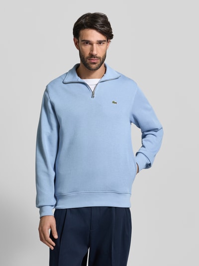 Männermodel trägt Regular Fit Troyer aus reiner Baumwolle von Lacoste in Hellblau, Strickstruktur, Logo-Patch, Ganzkörperansicht von vorne.