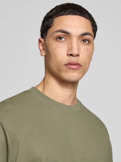 Mannenmodel draagt T-shirt met ronde hals model 'AUSTIN' van Jack & Jones in olijfgroen, elastische materiaalmix met katoen, recht model, detailopname bovenlichaam.