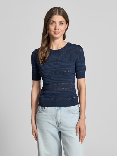 Frauenmodel trägt T-Shirt in Strick-Optik mit Rundhalsausschnitt von Guess, Material-Mix mit Viskose-Anteil, Körpernaher-Schnitt, dunkelblau, gemusterte Textur, gerippte-Abschlüsse, Ganzkörperansicht von vorne.