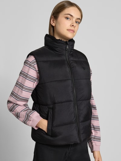 Frauenmodel trägt schwarze Regular Fit Weste in Stepp-Optik Modell 'BORG' von Superdry mit Stehkragen, Ganzkörperansicht von vorne.