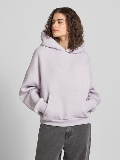 Frauenmodel trägt Relaxed Fit Sweatshirt mit Logo-Print von Review aus Baumwoll-Mix mit Logo-Stitching, Känguru-Tasche, elastische Abschlüsse, Ganzkörperansicht von vorne.