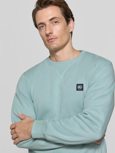Männermodel trägt Regular Fit Sweatshirt aus Baumwoll-Mix von LERROS in Hellblau mit Logo-Patch, Nahaufnahme Oberkörper.