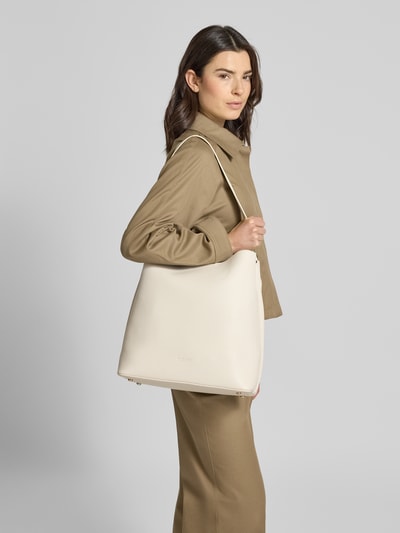 Frauenmodel trägt Tote Bag mit Reißverschlusstasche Modell 'Meloy' von Seidenfelt in Creme mit Strukturmuster, Logo-Prägung und abnehmbarem Schulterriemen, Hauptfach mit Magnetverschluss, Maße 34x34x17 cm, Länge Schulterriemen 67 cm, Nahaufnahme Oberkörper seitlich.