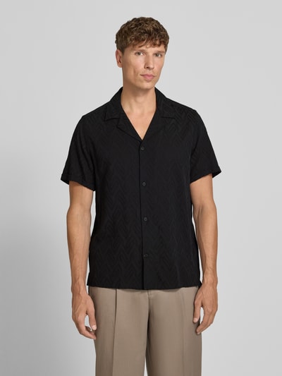 Männermodel trägt Regular Fit Freizeithemd aus Viskose-Baumwoll-Mix Modell 'Bijan' von DRYKORN in Schwarz mit Allover-Look, Knopfleiste, Reverskragen, Ganzkörperansicht von vorne, Rückenlänge 78 cm, Schulterbreite 45 cm, Ärmellänge 24 cm.