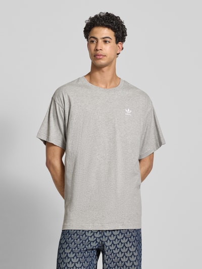 Männermodel trägt T-Shirt mit Label-Stitching von adidas Originals in Hellgrau, reine Baumwolle, Regular Fit, Nahaufnahme Oberkörper.