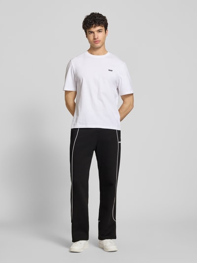 Mężczyzna nosi spodnie dresowe 'Sweatpants mit elastischem Bund und Logo' od REVIEW, bawełna, krój relaxed fit, logo, długość wewnętrzna nogawki 78 cm, widok całej sylwetki z przodu.
