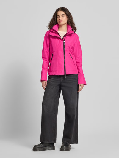 Frauenmodel trägt Windbreaker mit Zweiwege-Reißverschluss und Logo-Stitching von Superdry in Pink, Gerader-Schnitt, Seitliche Reißverschlusstaschen, Kapuze mit Kordelzug, Stehkragen, Ganzkörperansicht von vorne. Rückenlänge bei Größe S: 63 cm, Schulterbreite: 42 cm, Brustweite: 37 cm, Ärmellänge: 67 cm.