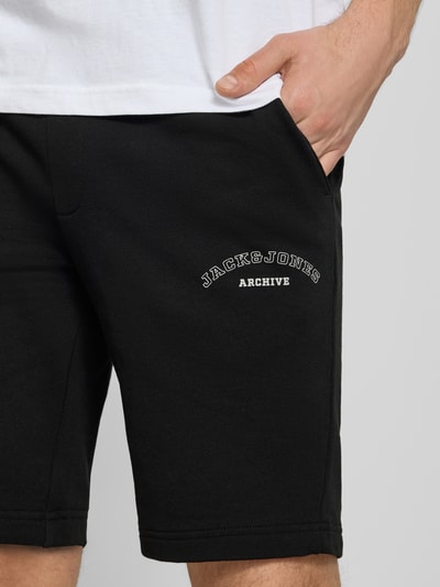 Männermodel trägt Shorts mit Logo-Print Modell 'GORDON' von Jack & Jones aus schwarzem Baumwoll-Mix, Relaxed-Fit, Nahaufnahme Oberschenkel.