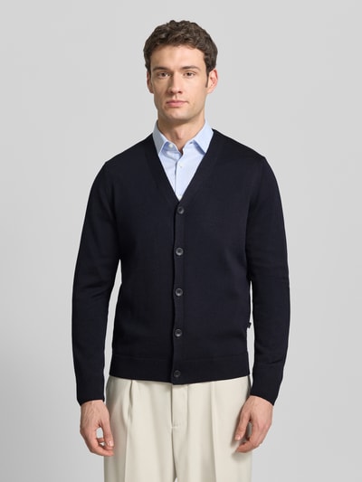 Männermodel trägt Cardigan aus Schurwolle mit V-Ausschnitt von MAERZ, Regular-Fit, schwarze Farbe, sichtbare Knopfleiste, Ganzkörperansicht von vorne.