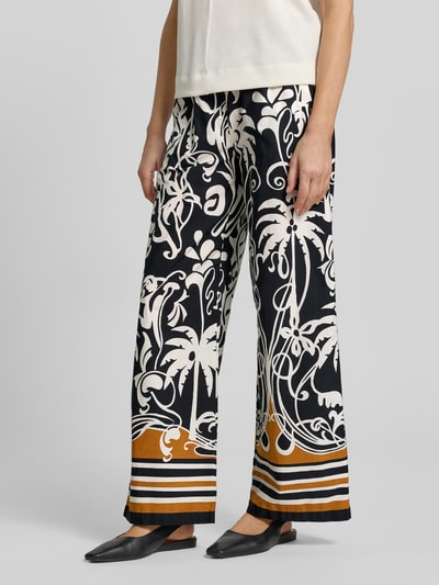 Frauenmodel trägt Wide Fit Stoffhose mit floralem Allover-Print von Emily Van den Bergh in Schwarz, Weiß und Braun aus reiner Baumwolle mit elastischem Bund, Ganzkörperansicht von vorne.