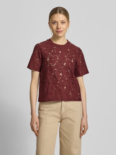 Modelka kobieca ma na sobie Regular Fit T-Shirt aus Spitze Modell 'SALLIE' od Vero Moda w kolorze bordowym z koronkowej bawełnianej mieszanki, klasyczny krój regular fit, krótki rękaw, dekolt okrągły, wygląd jednokolorowy, widok całej sylwetki z przodu.