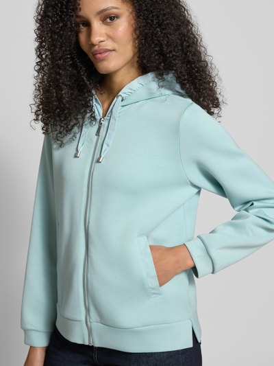 Kobiece model nosi Regular Fit Sweatjacke mit Viskose-Anteil od Tom Tailor, jednolity kolor, krój regular fit, zamek błyskawiczny, nadruk z logo na tunelu, kaptur z tunelem, długi rękaw, wykończenie z bocznymi rozcięciami, boczne kieszenie listewkowe, zdjęcie półzbliżeniowe z przodu.