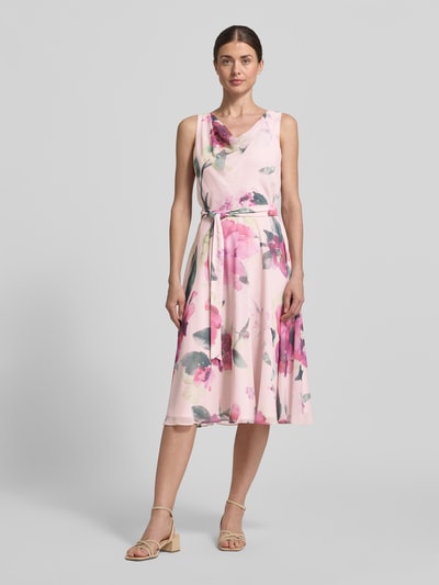 Frauenmodel trägt Knielanges Cocktailkleid mit Bindegürtel von Vera Mont aus Chiffon, Taillierter Schnitt, Wasserfall-Ausschnitt, rosa mit Blumenmuster, Knielänge, Ganzkörperansicht von vorne. Brustweite 40 cm, Rückenlänge 104 cm bei Größe 36.