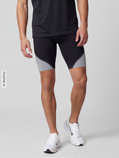 Männermodel trägt Slim Fit Sportshorts mit Logo-Print von Under Armour, schwarz-grau mit glatter Textur, Ganzkörperansicht von vorne, KI-modifiziertes Bild.