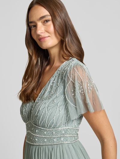 Frauenmodel trägt Abendkleid mit Paillettenbesatz von Christian Berg Cocktail aus Chiffon in zartem Grün mit Schmetterlingsärmel, Nahaufnahme Oberkörper.