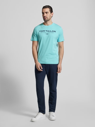 Männermodel trägt Regular Fit T-Shirt aus reiner Baumwolle von Tom Tailor, unifarben, Rundhals, Label Print, Ganzkörperansicht von vorne.