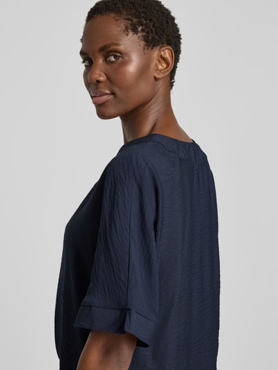 Frauenmodel trägt Blusenshirt mit V-Ausschnitt von Christian Berg Woman in Dunkelblau, strukturierte Textur, 1/2-Arm, Detailaufnahme Rückenansicht. Regular Fit, Rückenlänge 31 cm bei Größe 36, Ärmellänge 61 cm bei Größe 36.