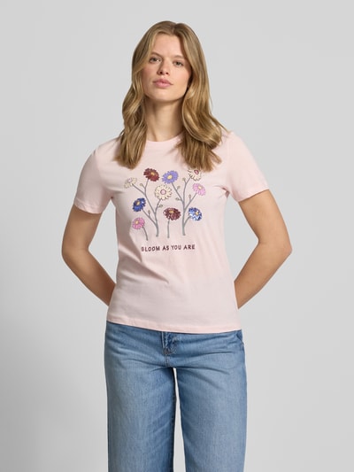 Frauenmodel trägt Slim Fit T-Shirt aus reiner Baumwolle Modell 'KITA' von Only, Optik: unifarben, Motiv-Print mit Pailletten, Rundhals, Kurzarm, Materialverarbeitung: Jersey, zartrosa Farbe, glatte Textur, Ganzkörperansicht von vorne.