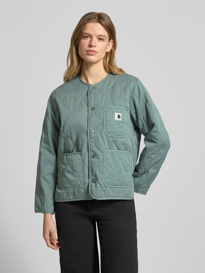 Vrouwenmodel draagt Steppjacke mit Label-Detail Modell 'Kylan' van Carhartt Work In Progress in groen katoen, relaxed fit, opgestikte zakken, ronde hals, knoopsluiting, detailopname bovenlichaam.