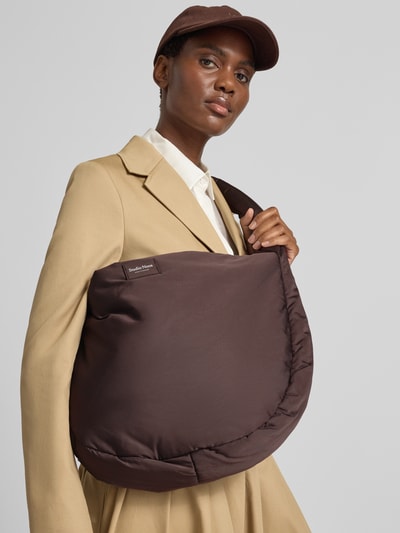 Vrouwenmodel draagt Shoulder Bag met logo-detail Model 'Puffy' van Studio Noos, bruin, hoofvak met ritssluiting, schouderband, breedte 48 cm, lengte 35 cm, diepte 10 cm, bandlengte 78 cm, half-close-up voorkant