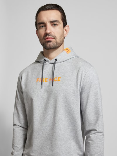 Męski model nosi szarą bluzę z kapturem z logo FIRE + ICE, model 'CADELL', krój regular fit, detal z logo, zbliżenie na górną część ciała