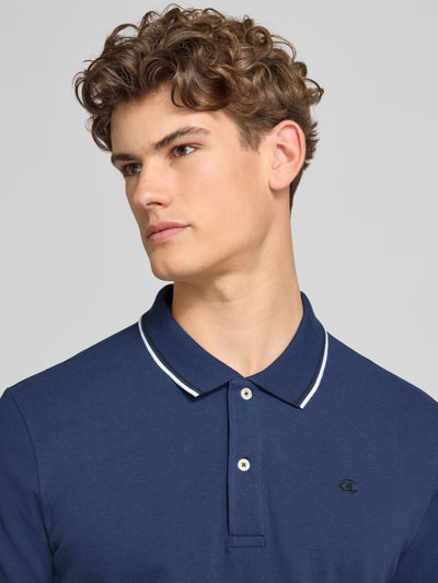 Mężczyznamodel nosi Slim Fit Poloshirt mit Label-Stitching von CHAMPION z bawełny, krój slim fit, listwa guzikowa, zbliżenie na górę ciała.