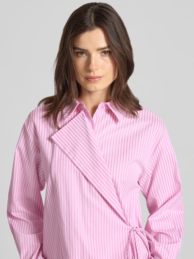 Frauenmodel trägt Regular Fit Hemdbluse mit Viskose-Anteil Modell 'WITO' von YAS, rosa-weiß gestreift, Wickel-Optik, Nahaufnahme Oberkörper.