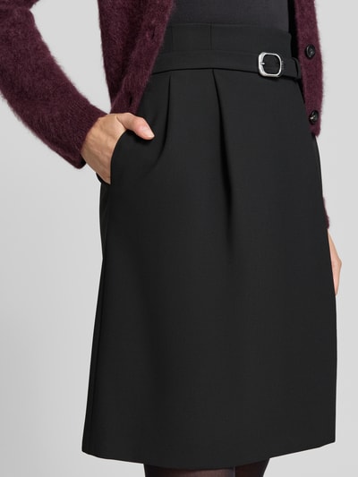 Vrouwenmodel draagt zwarte knielange rok met bandplooien, mat oppervlak, Knielanger Rock mit Bundfalten Modell 'Ralema' van HUGO, detailopname bovenbeen, Dames Knielanger Rok van HUGO.