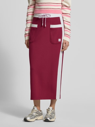 Frauenmodel trägt Straight Fit Midirock mit Logo-Print von Marc Cain in Dunkelrot mit AufgesetzteTaschen, elastischem Bund mit Tunnelzug, Ganzkörperansicht von vorne.