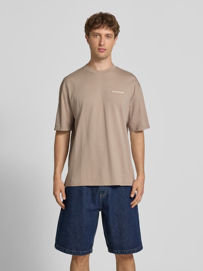 Männermodel trägt Oversized T-Shirt mit Label-Stitching von Pegador in Beige aus Baumwoll-Mix, Rundhalsausschnitt, Ganzkörperansicht von vorne.