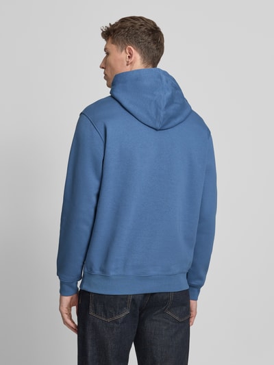 Männermodel trägt Hoodie mit Kängurutasche von GAP in Blau, lockere passform, gerippte Abschlüsse, Rückenansicht, Ganzkörperansicht Rückansicht.