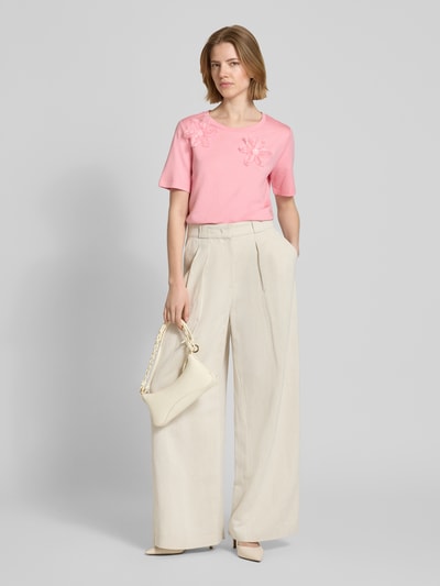 Frauenmodel trägt Regular Fit T-Shirt mit floralem Zierbesatz von monari aus Baumwoll-Modal-Mix in Rosa, Rundhalsausschnitt, hellbeige weite Hose, Tasche, Ganzkörperansicht von vorne, Rückenlänge bei Größe 36: 59 cm.
