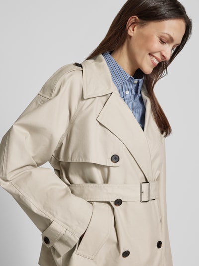 Modelka nosi Regular Fit Trenchcoat aus Baumwoll-Lyocell-Mix von Marc O'Polo, efekt: jednolity kolor, krój regular fit, kołnierz z połami, listwa guzikowa 2-rzędowa, pasek w talii, długi rękaw z patkami, wpuszczane kieszenie, materiał: mieszanka bawełny i lyocellu. Zbliżenie na górną część ciała.