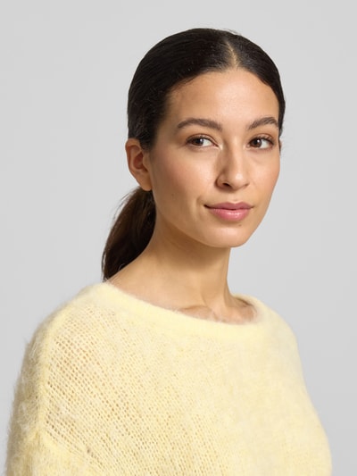 Modelka kobieca nosi Strickpullover mit gerippten Abschlüssen Modell 'NIBY' od American Vintage, mieszanka alpaki z dodatkiem stretchu, luźny krój, kremowożółty kolor, okrągły dekolt, wyraźna faktura dzianiny, kontekst: długość tyłu w rozm. S 56 cm, długość rękawa 65 cm, ujęcie: zbliżenie na górną część sylwetki z przodu.