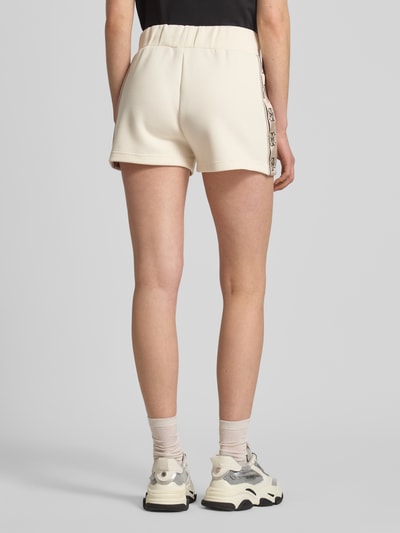 Frauenmodel trägt Shorts mit Kordelzug und Logo-Print Modell 'BRITNEY' von Guess Activewear in Creme, Loose Fit, Ganzkörperansicht Rückansicht.