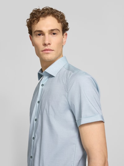 Männermodel trägt Slim Fit Business-Hemd mit Kentkragen von OLYMP Level Five, hellblau, glatte Textur, Nahaufnahme Oberkörper. Baumwoll-Elasthan-Mix, kurze Ärmel, Knopfleiste.