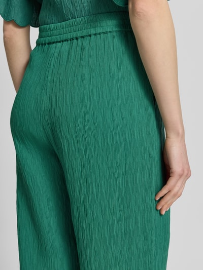 Frauenmodel trägt Stoffhose aus Viskose-Mix mit Wellensaum von JAKE*S STUDIO WOMAN in Grün mit Strukturmuster, Detailaufnahme Rückansicht. Damen Stoffhose, Wide Leg Fit, elastischer Bund, Bundweite 35 cm, Innenbeinlänge 67 cm, Größe 36.